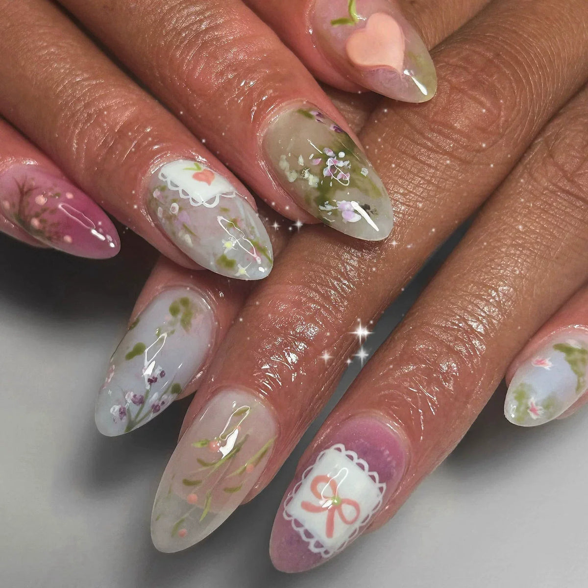 Gros plan d'une main montrant des ongles press-on roses à l'amande française avec de délicats accents floraux.