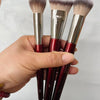 Une main tient trois pinceaux de maquillage à fondation liquides inclinés avec des ferrules argentées et des poils roses et d