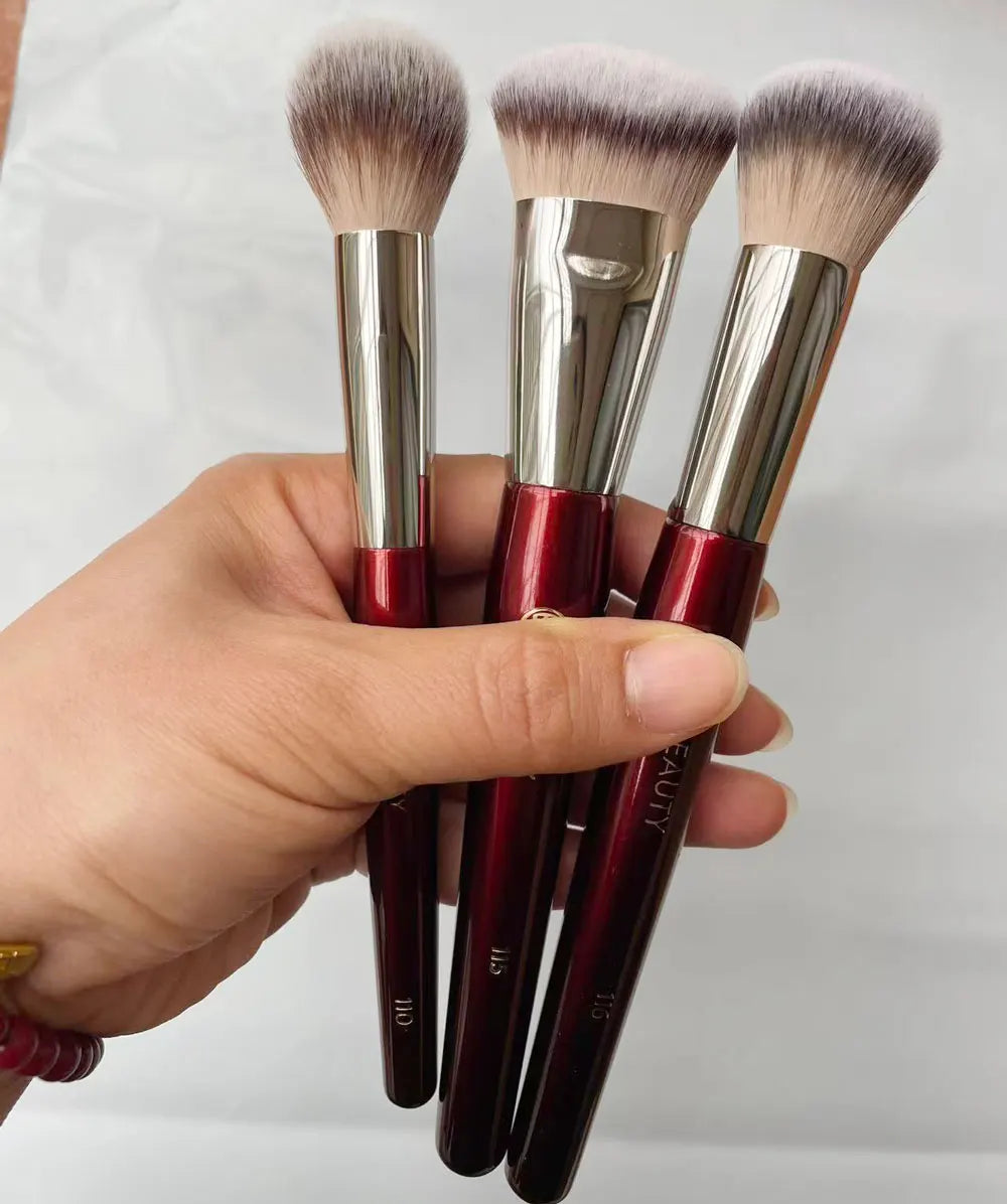 Une main tient trois pinceaux de maquillage à fondation liquides inclinés avec des ferrules argentées et des poils roses et d