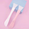 A pair of pink and white silicone facial mask brushes are shown next to a light blue box.