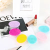 A collection of pink, purple, yellow, and blue silicone facial cleansing brushes displayed on a white surface.