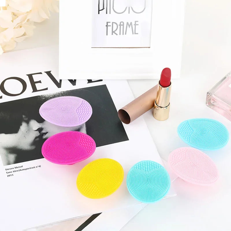 A collection of pink, purple, yellow, and blue silicone facial cleansing brushes displayed on a white surface.