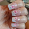 A close-up of a hand displaying press-on acrylic flower nails with pink and white floral designs.