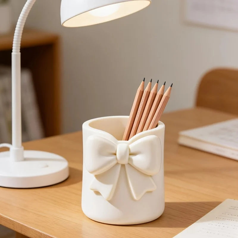 Un organisateur de rangement décoratif blanc en forme de nœud tient plusieurs crayons de bois sur un bureau en bois clair.