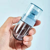 A hand holds a clear, portable refillable fine mist spray bottle with a blue cap and nozzle.