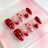 A set of red and pink Y2K almond press-on nails with a hand-painted floral design displayed on a clear acrylic tray.