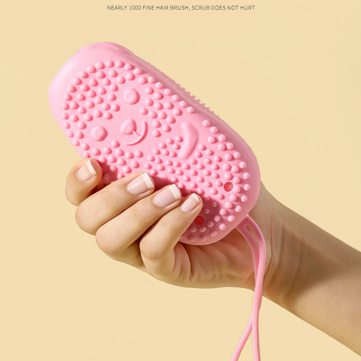 A hand holds a pink silicone body brush with small bumps, demonstrating its use for gentle exfoliation.