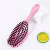 A pink bristle hollow arc styling comb resting on a white surface next to a slice of lime.