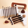 A set of thirteen professional makeup brushes in brown and black with a leather storage case and white background.