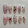 A collection of 24 pink heart pearl press-on fake nails featuring various designs including glitter and floral accents.