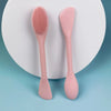 A pink double head silicone face cleansing brush resting on a white circular background.
