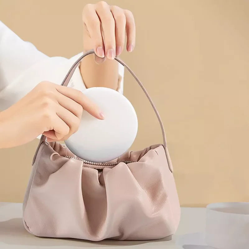 A hand is placing a white LED makeup mirror into a light pink cosmetic bag.