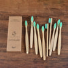 A set of ten natural bamboo toothbrushes with green bristles displayed on a wooden surface.