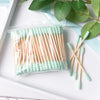 Bâtonnets de cotons en bambou avec des pointes vert clair et des tiges en bois naturel, posés sur une surface blanche