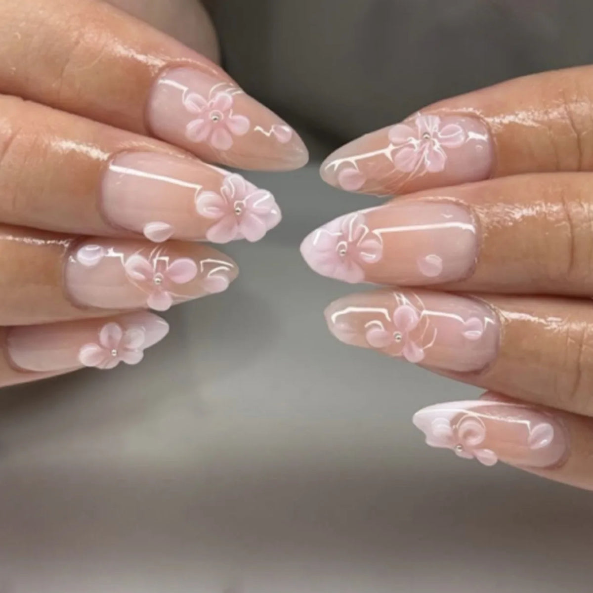 Gros plan sur des mains montrant des ongles press-on en forme d'amande décorés de délicats motifs floraux roses.