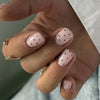 Close-up of a hand displaying reusable pink press-on nails with small black polka dots on an almond shape.