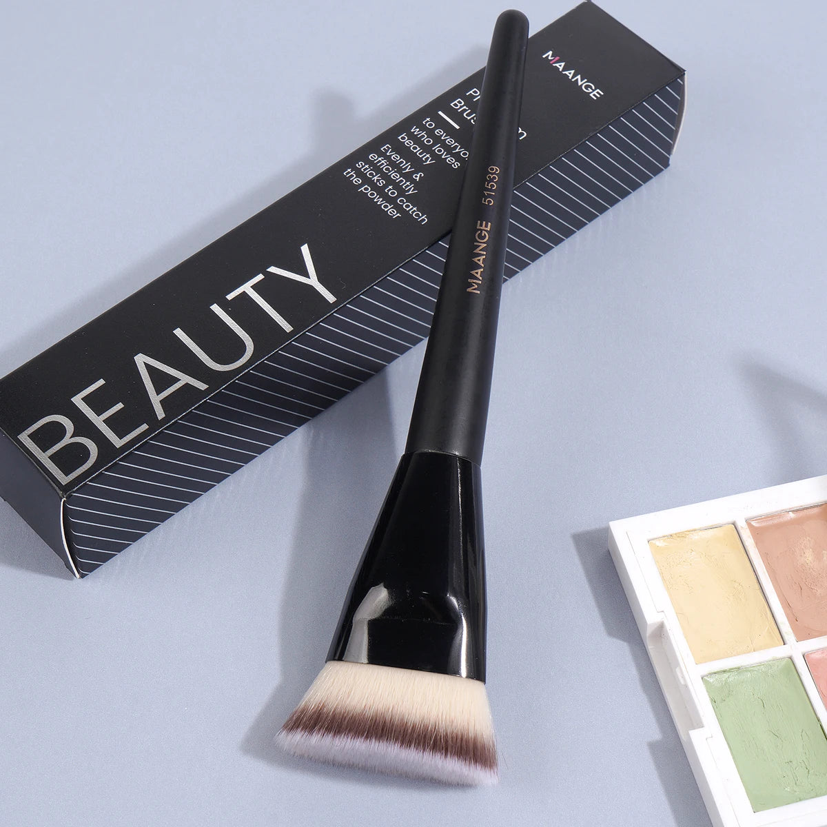 A black flat kabuki foundation brush is shown next to its packaging box.