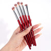 A hand holds a set of red precision makeup brushes with silver ferrules against a white background.