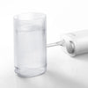 A clear cylindrical oral irrigator device is shown next to its white charging or power unit.