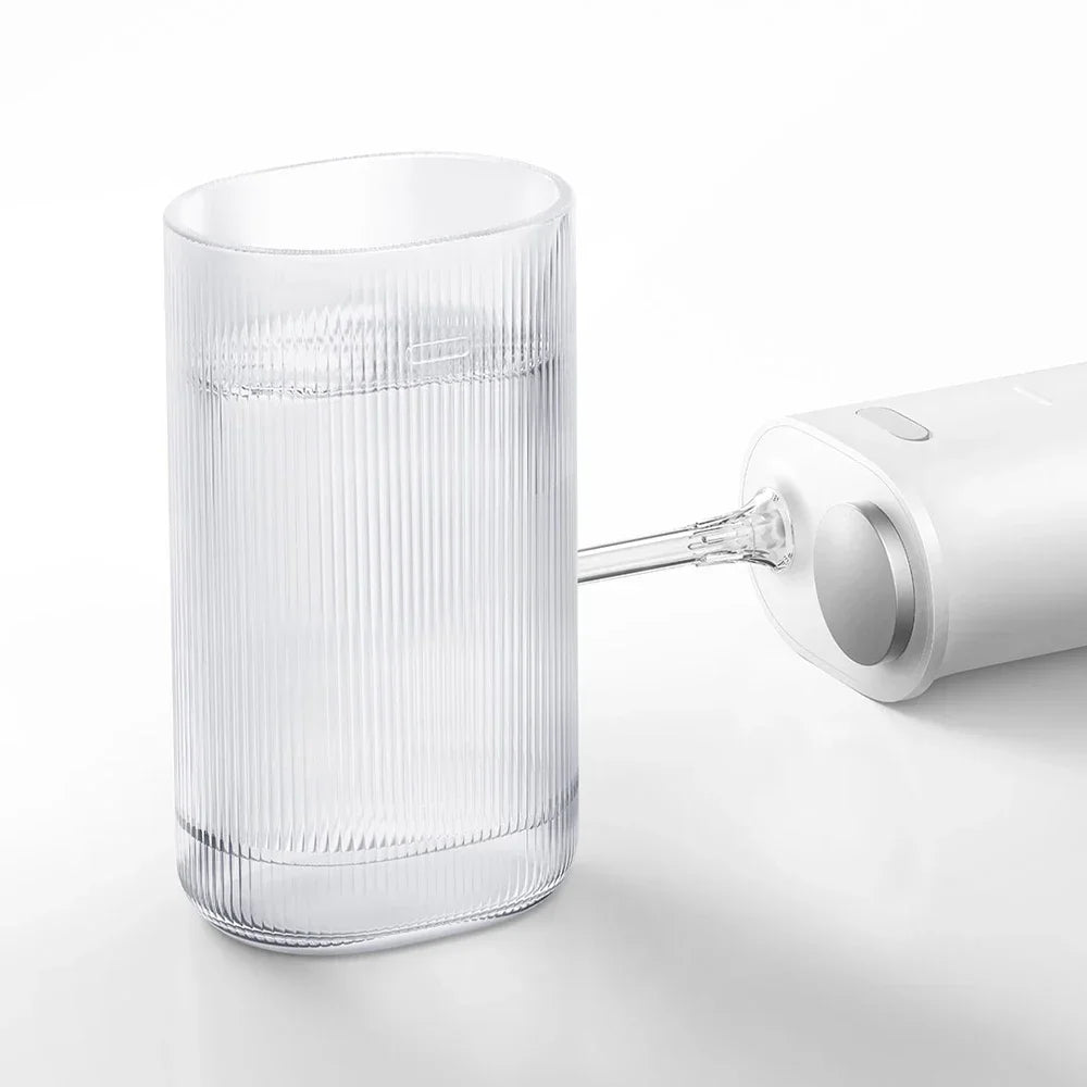 A clear cylindrical oral irrigator device is shown next to its white charging or power unit.