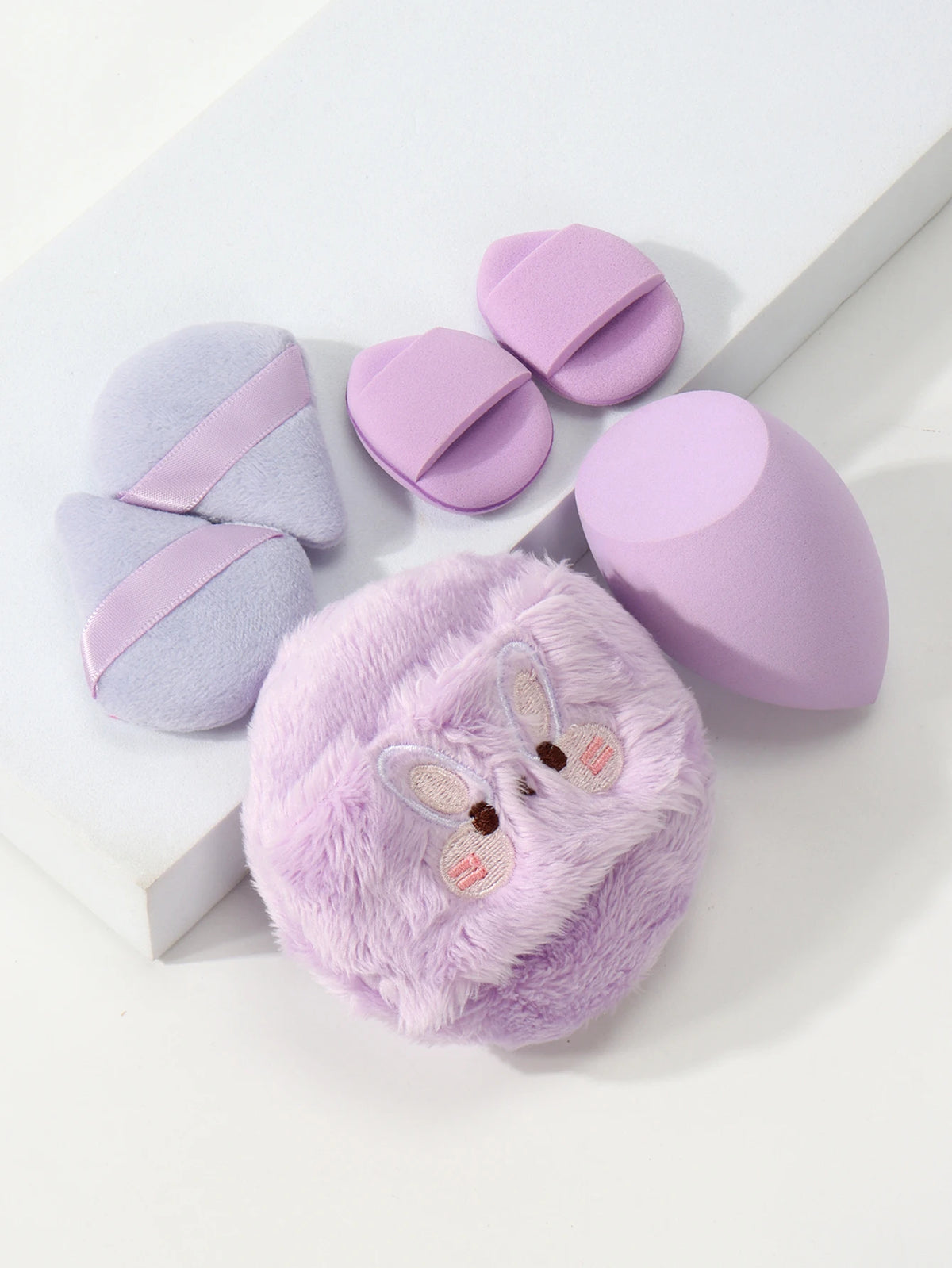 Un ensemble de poudres légères brodées dans des tons de lavande et de lilas posés sur une surface blanche.