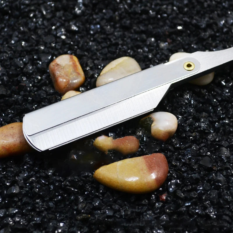 A silver straight edge barber razor resting on black volcanic rock with several polished stones.
