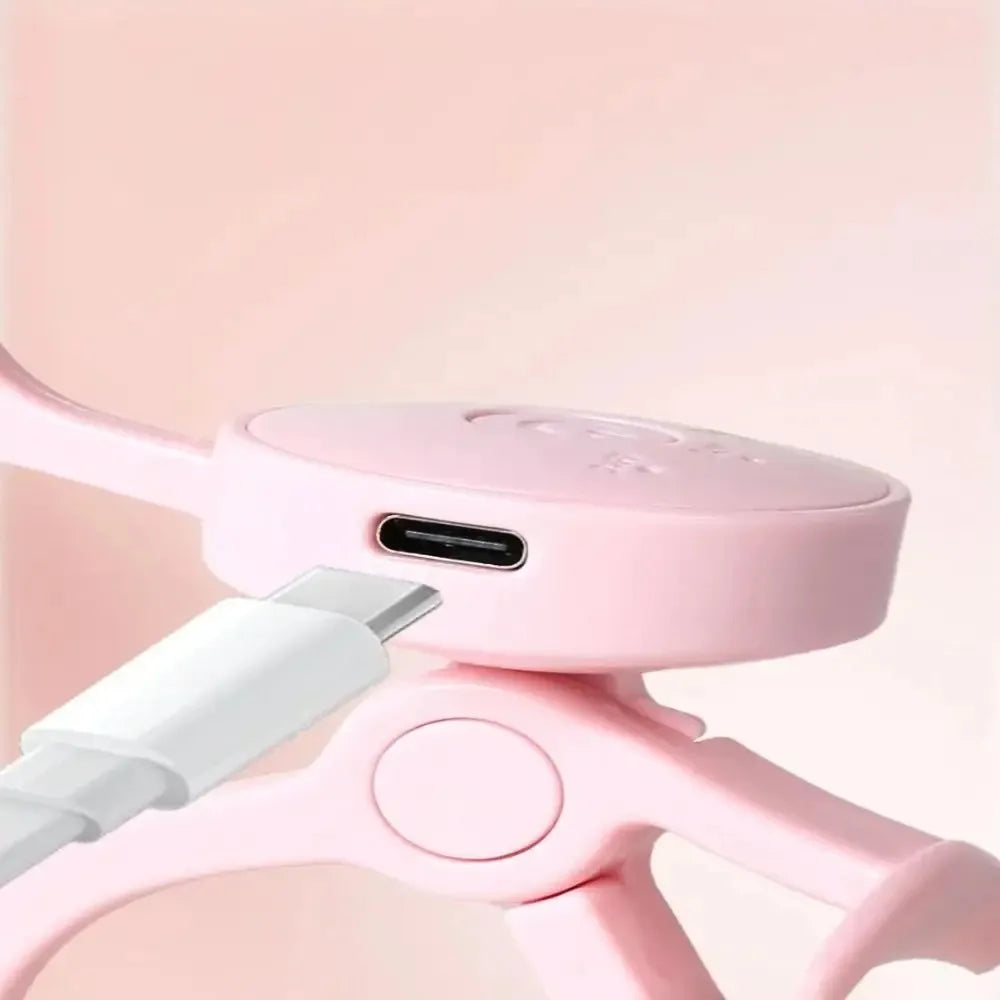A pink frameless heated eyelash curler with a white handle is shown against a light background.