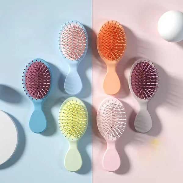 A collection of colorful mini detangling hair brushes and massagers displayed on a light blue and pink background.