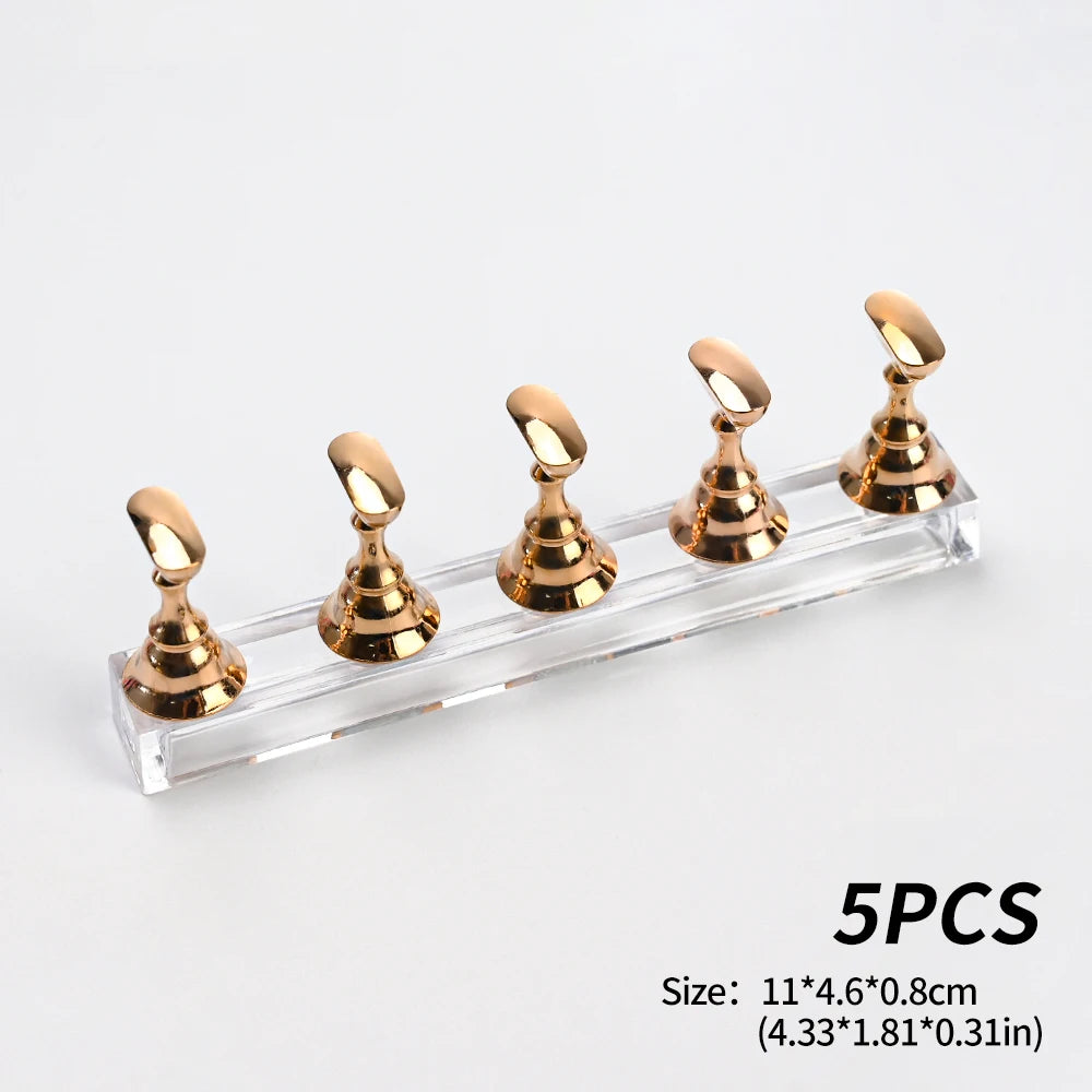 Un ensemble de cinq supports à ongles magnétiques dorés métalliques sur une base en acrylique transparent.