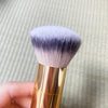 A close-up of a fluffy, tapered bamboo airbrush foundation and bronzer brush with a lavender-gray bristles set against a ligh
