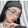 A woman wearing a black knit headband and purple-tinted retro frameless reading glasses.