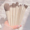 A hand holds a set of ten professional makeup brushes with light beige handles and natural hair bristles.