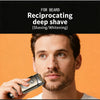 A man is using a portable electric foil shaver on his beard.