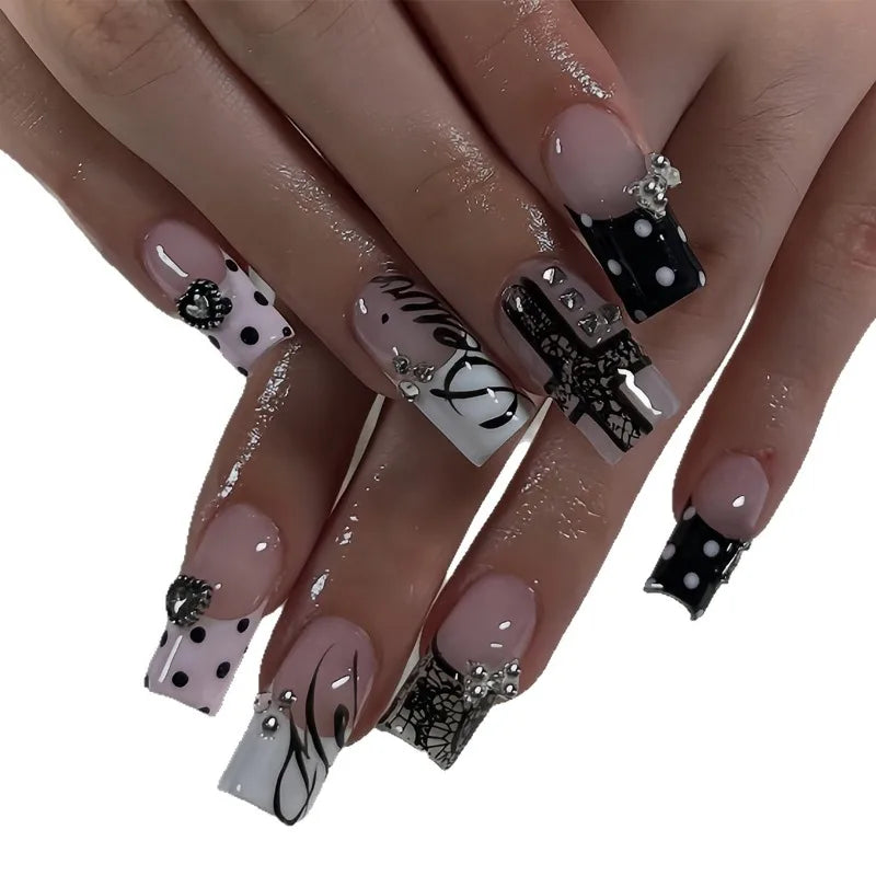 A hand displaying gothic Y2K press-on nails featuring black and white designs with cross and bow motifs.