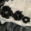 Scrunchies en satin de chiffon noirs de différentes tailles posés sur du papier de soie blanc