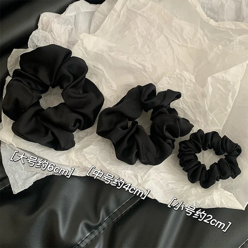 Scrunchies en satin de chiffon noirs de différentes tailles posés sur du papier de soie blanc