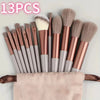 A set of 13 professional makeup brushes in various shades of pink and taupe are displayed on a pink towel.