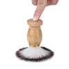A hand is holding a men's shaving set featuring a wooden handle and a brush with dark and light bristles.