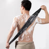 A person is using a black exfoliating loofah to scrub their back with soap in a studio setting.