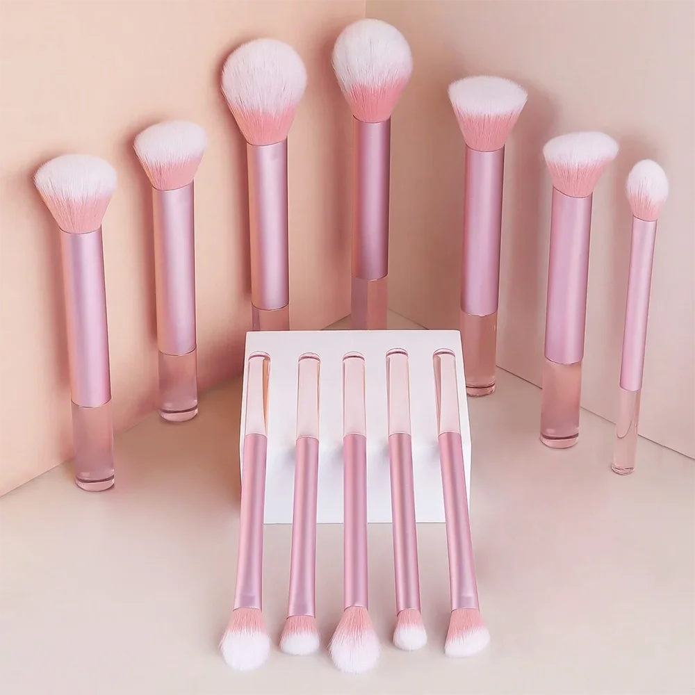 A collection of pink and white makeup brushes and puffs displayed upright in a row against a light background.