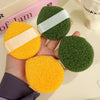 A hand holds two exfoliating cleansing sponges, one yellow and one green, for blackhead removal.
