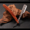 A professional wood handle shaving razor with a dark brown wooden handle and a silver blade resting on a piece of bark.