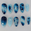Eine Sammlung blauer durchscheinender Press-on-Falschnägel in Form von Mandelblumen mit filigranen Designs und Glitzerakzente