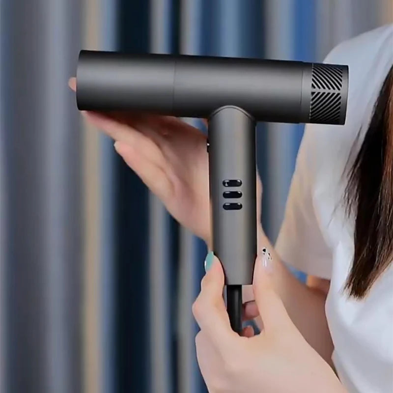 A hand holds a black professional electric hair dryer for barbers, showing the device's design.