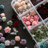 A collection of pink, red, and green rose-shaped pearl nail art charms in various shades displayed in a clear plastic contain