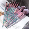A set of ten professional makeup brushes with iridescent pink and green bristles displayed on a magazine page.