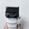 A close-up of a black professional hair clipper blade with a white body being held in a hand.