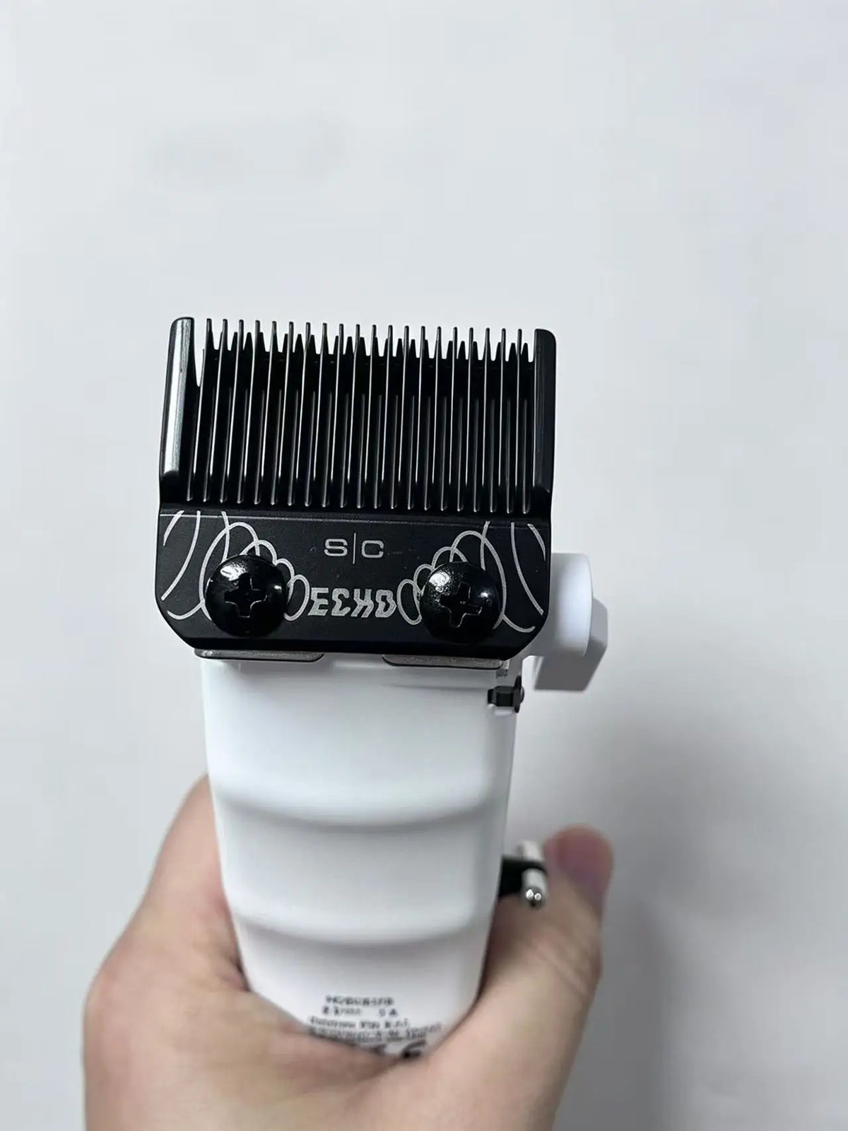 A close-up of a black professional hair clipper blade with a white body being held in a hand.
