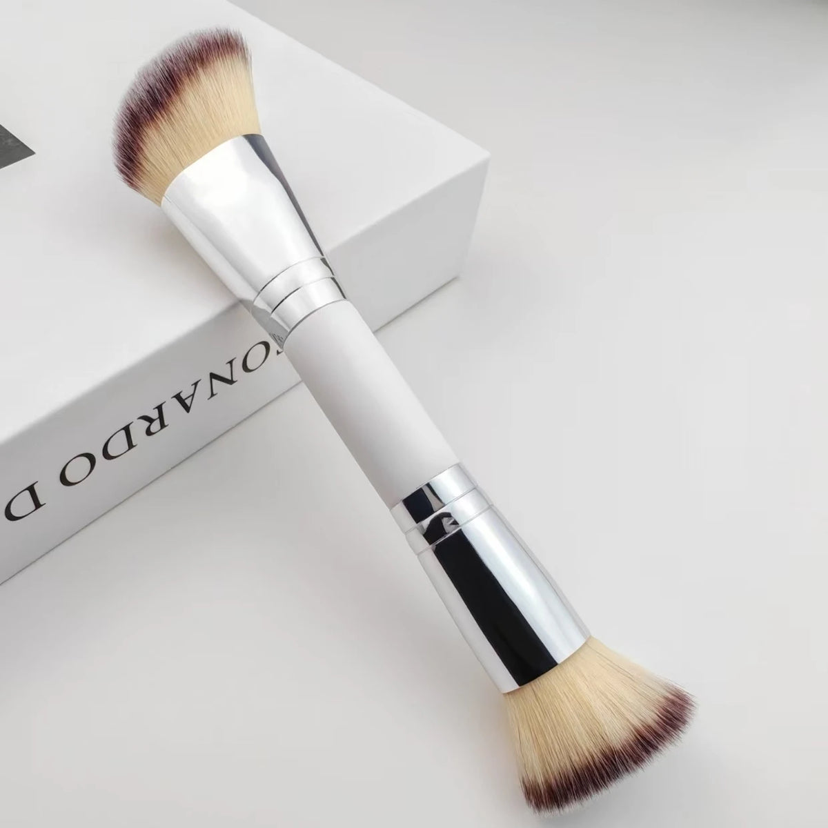 Silberner Make-up-Pinsel mit natürlicher Haarkugel auf einer weißen Box.