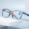 Pair of blue-tinted reading glasses with a marbled frame resting on a white surface.